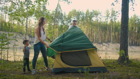 man-and-woman-is-pitching-a-tent-in-forest-little-son-is-helping-them-family-trip-at-nature-at-summer